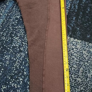 Pode incluir: Uma camisola de cor bord&ocirc; com uma fita m&eacute;trica amarela ao lado. A fita indica medidas em cent&iacute;metros, com o comprimento da pe&ccedil;a a atingir cerca de 76 cm.