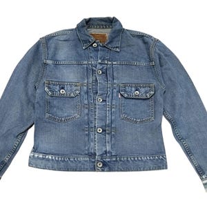 Op de afbeelding: Een lichtblauwe spijkerjas met twee borstzakken en twee zijzakken. De jas heeft een knoopsluiting aan de voorkant, een kraag en lange mouwen. De denim heeft een verweerde uitstraling. Een klein bruin label is zichtbaar op de achterkant van de kraag.