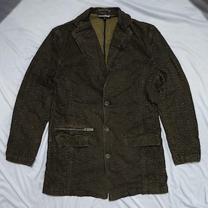 Op de afbeelding: Een donkerbruine blazer met een subtiel textuurpatroon, een ingekeepte revers en een sluiting met drie knopen aan de voorzijde. Het kledingstuk heeft een borstzak met rits aan de rechterkant, een klepzak aan de linkerkant en een contrasterende olijfgroene voering.
