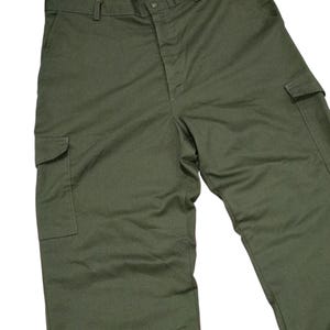 May include: Olive green cargo trousers with multiple pockets and a button closure. The trousers have a classic, utilitarian design, suitable for various activities. The fabric appears to be a durable material, ideal for outdoor wear.