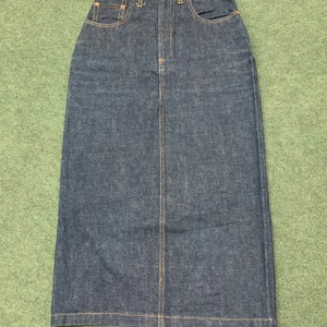 Pu&ograve; includere: Una gonna in denim blu scuro con vita alta e silhouette dritta e lunga. La gonna ha una chiusura con bottone e zip sul davanti e cinque tasche.