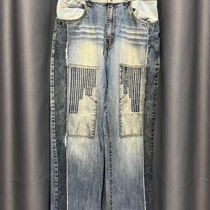 May include: Blue denim jeans with a patchwork design. The jeans have a light wash and are distressed with rips and tears. The jeans have a wide leg and are made of a soft, comfortable fabric.