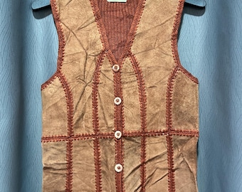 Könnte beinhalten: Eine Vintage-Weste aus braunem Wildleder mit einem gestrickten braunen Kragen und Rücken. Die Weste hat ein Patchwork-Design mit dekorativen Nähten und weißen Knöpfen auf der Vorderseite. Das Etikett lautet "Christina".