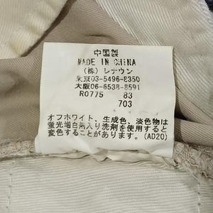 May include: A close-up of a tag with Japanese text, including the words "MADE IN CHINA." The tag is attached to beige fabric. The text also includes a warning about using fluorescent whitening agents.