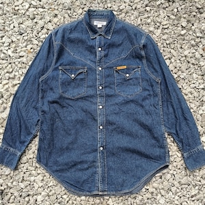 Pode incluir: Camisa de ganga de manga comprida em lavagem azul m&eacute;dia. A camisa tem uma frente abotoada, dois bolsos no peito e uma gola cl&aacute;ssica. A camisa tem um jugo de estilo ocidental e &eacute; feita de tecido de ganga dur&aacute;vel.