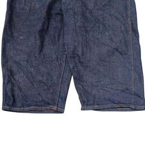 May include: Close-up of dark blue denim shorts. The shorts have a classic design with visible stitching and a slightly faded appearance. The fabric shows subtle texture and creases.