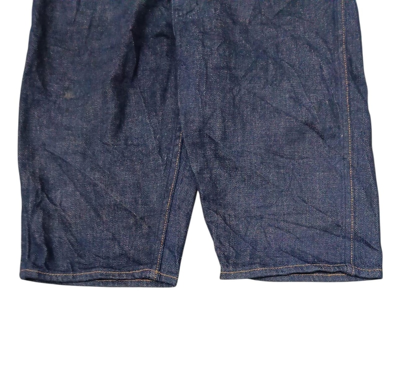 May include: Close-up of dark blue denim shorts. The shorts have a classic design with visible stitching and a slightly faded appearance. The fabric shows subtle texture and creases.