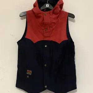 May include: A sleeveless vest with a red hood and upper chest panel, and a navy blue lower section. The vest has a button-up front and a small patch on the lower left side. The vest is hanging on a black hanger.