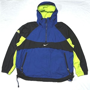 Puede incluir: Una chaqueta con capucha en azul, negro y amarillo neón que presenta un cierre de media cremallera, un logotipo Nike blanco en el pecho y un logotipo ACG en el hombro derecho. La chaqueta incluye dos bolsillos delanteros con cremallera.