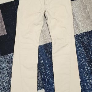 May include: Beige trousers with a classic design. The trousers feature a button and zip closure, along with two zipped front pockets. They are made from a lightweight fabric and have a straight leg cut.