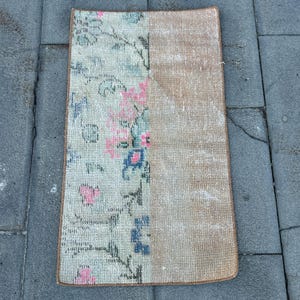 May include: A rectangular rug featuring a split design. The left side displays a light background with a floral pattern in shades of pink, blue, and dark gray. The right side is a solid, textured tan color. The entire rug has a finished brown border.