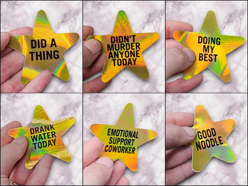 May include: Six gold holographic star-shaped stickers with different humorous phrases printed on them. The phrases are "Did a thing", "Didn't murder anyone today", "Doing my best", "Drank water today", "Emotional support coworker", and "Good noodle".