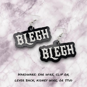 以下が含まれることがあります： 黒いアクリル製のイヤリングで、白いゴシック様式の文字で「BLEGH」という言葉が書かれています。イヤリングには銀色のイヤーフックが付いています。画像には、イヤーフック、クリップオン、レバーバック、腎臓ワイヤー、スタッドなどのハードウェアオプションも表示されています。