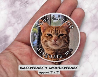 Puede incluir: Una pegatina circular con la fotografía de un gato atigrado naranja con expresión severa. El texto "Your AI slop disgusts me" está impreso en letras mayúsculas negras alrededor de la cabeza del gato. La pegatina mide unos 5 cm por 5 cm.