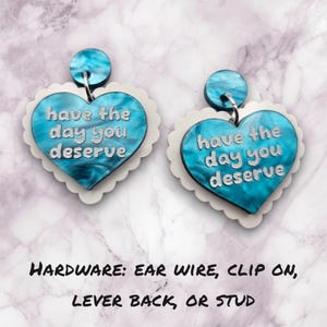 Pode incluir: Um par de brincos em forma de cora&ccedil;&atilde;o azul e branco com o texto "have the day you deserve" em cada brinco. Os brincos est&atilde;o dispon&iacute;veis com fecho de fio, fecho de clip, fecho de alavanca ou fecho de bot&atilde;o.