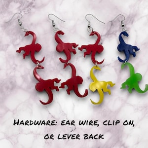 Puede incluir: Cuatro pares de pendientes colgantes con tres siluetas de monos superpuestas. Los pendientes están disponibles en rojo, amarillo, verde y azul.  HARDWARE: EAR WIRE, CLIP ON, OR LEVER BACK