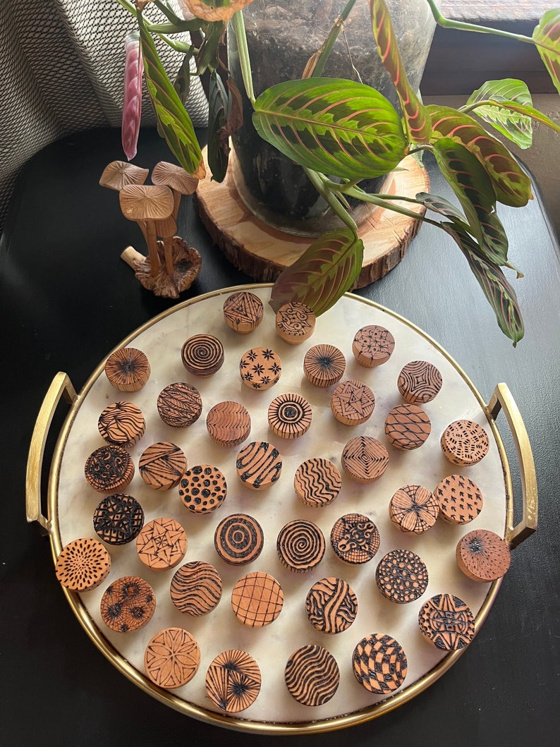 K&ouml;nnte beinhalten: Ein Tablett mit 25 Holzgriffen mit verschiedenen schwarz-wei&szlig;en Mustern. Die Griffe sind kreisf&ouml;rmig auf einem wei&szlig;en Marmortablett mit goldenem Rand angeordnet.