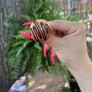 May include: A wooden button with a brown background and black wavy lines. The button is round and has a smooth surface.