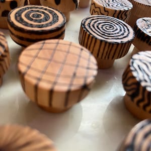 K&ouml;nnte beinhalten: Eine Sammlung von Holzkn&ouml;pfen mit verschiedenen geometrischen Mustern in Schwarz und Wei&szlig;. Die Kn&ouml;pfe sind rund und haben eine glatte, polierte Oberfl&auml;che.