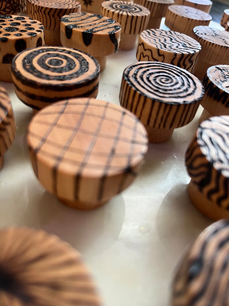 K&ouml;nnte beinhalten: Eine Sammlung von Holzkn&ouml;pfen mit verschiedenen geometrischen Mustern in Schwarz und Wei&szlig;. Die Kn&ouml;pfe sind rund und haben eine glatte, polierte Oberfl&auml;che.