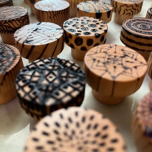 K&ouml;nnte beinhalten: Nahaufnahme einer Sammlung von Holzkn&ouml;pfen mit verschiedenen schwarzen und wei&szlig;en geometrischen Mustern, die in die Oberfl&auml;che gebrannt sind.