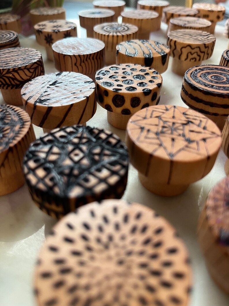 K&ouml;nnte beinhalten: Nahaufnahme einer Sammlung von Holzkn&ouml;pfen mit verschiedenen schwarzen und wei&szlig;en geometrischen Mustern, die in die Oberfl&auml;che gebrannt sind.