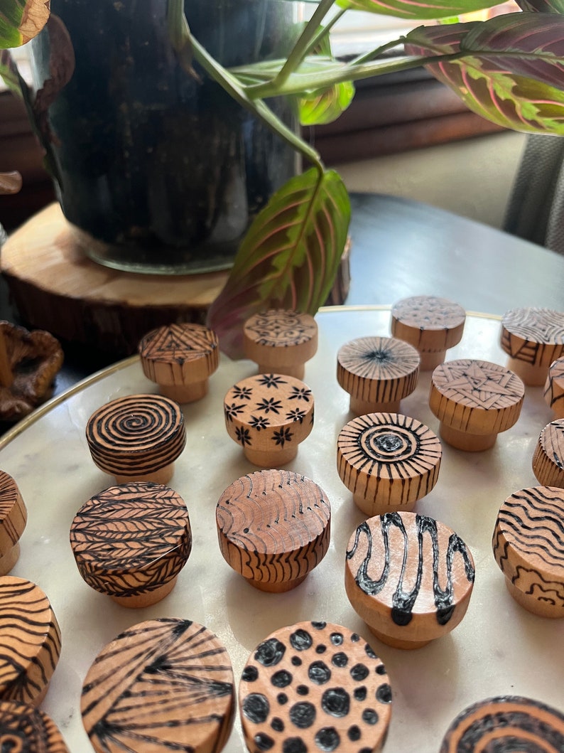 K&ouml;nnte beinhalten: Eine Sammlung von 15 Holzgriffen mit verschiedenen geometrischen Mustern in Schwarz und Wei&szlig;. Die Griffe sind rund und haben eine nat&uuml;rliche Holzoptik.