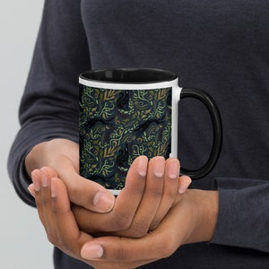 May include: A black and white coffee mug with a black handle. The mug has a dark blue background with a pattern of black squirrels, green leaves, and brown branches.