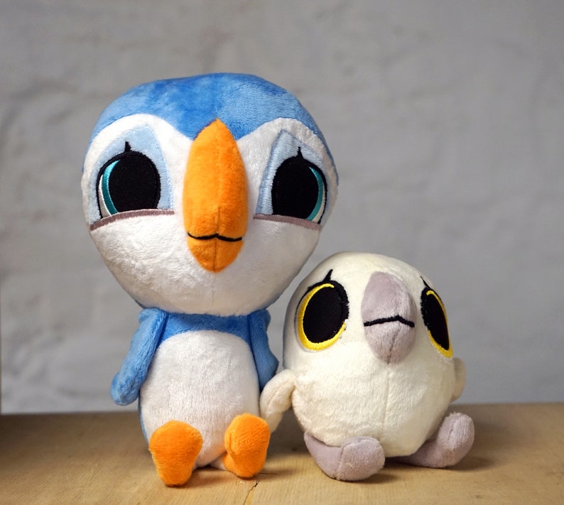 May include: Two plush toys, one blue and white penguin with an orange beak and the other a white bird with a gray beak and yellow eyes.