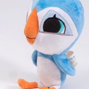 May include: A blue and white plush toy shaped like a puffin with orange feet and beak. The toy has large black eyes with blue accents and a white face. The toy is sitting on a white surface.