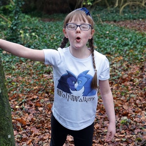 May include: A young person wearing a white t-shirt with a blue and black wolf graphic and the text "Wolfwalkers" on it. They are wearing glasses and have their hair in two braids.