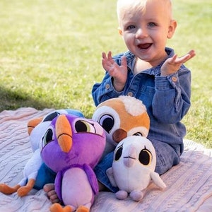 May include: A child plays with four plush toys. The toys are a purple bird, a white bird, a brown owl, and a blue bird. The toys are all soft and cuddly.
