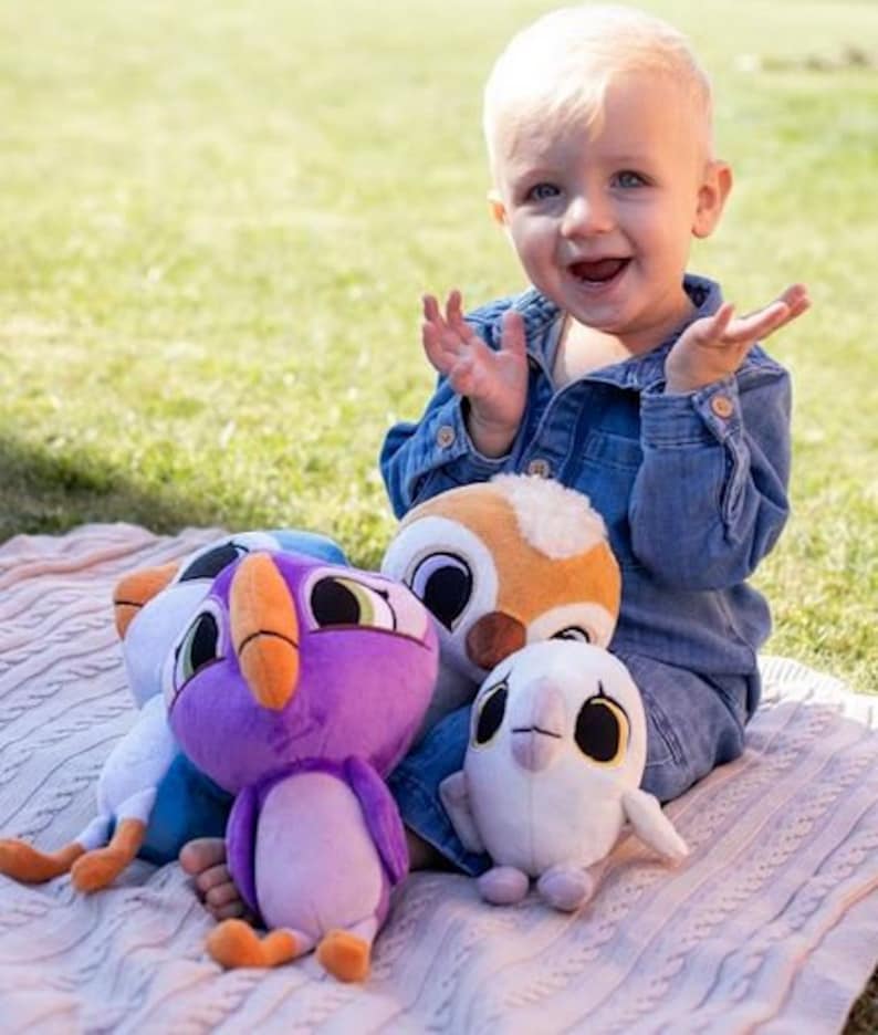 May include: A child plays with four plush toys. The toys are a purple bird, a white bird, a brown owl, and a blue bird. The toys are all soft and cuddly.