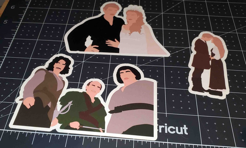 May include: Four illustrated stickers featuring characters from the movie 'The Princess Bride'. The stickers are on a black and white cutting mat. The stickers are white with a white outline. The first sticker shows a man and a woman in wedding attire. The second sticker shows a man with long dark hair and a brown jacket. The third sticker shows a man with a green shirt and a sword. The fourth sticker shows a man with a brown shirt and a belt.