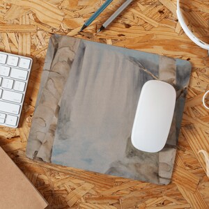 May include: A watercolor painting of a waterfall with a white mouse pad on a wood surface.