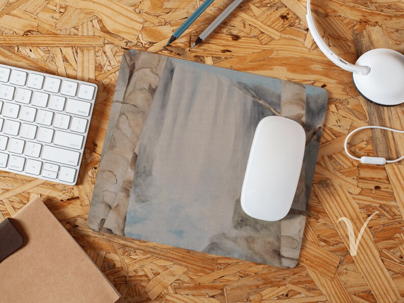 May include: A watercolor painting of a waterfall with a white mouse pad on a wood surface.