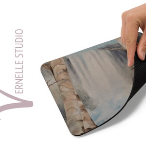 May include: A mouse pad with a watercolor painting of a waterfall and trees. The back of the mouse pad is black.