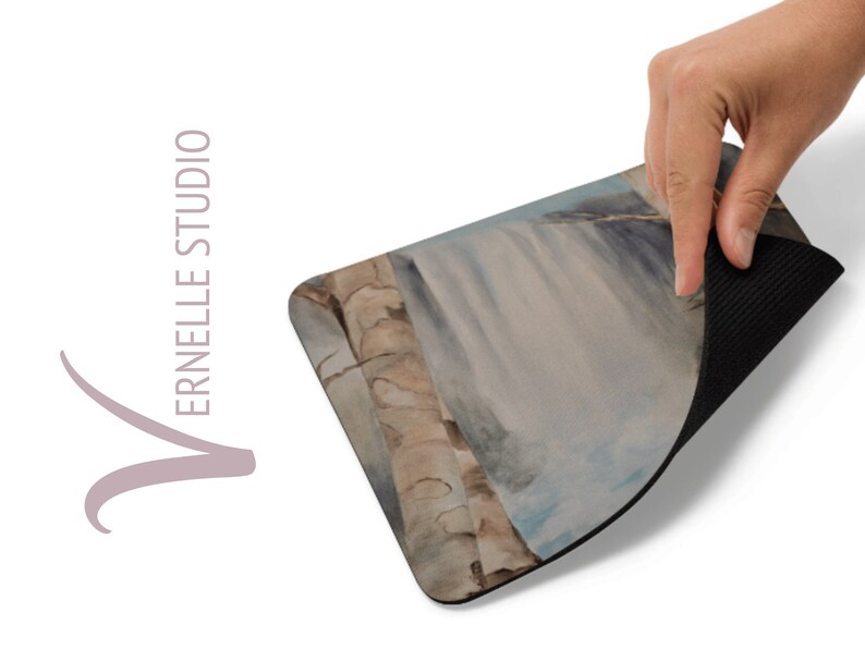 May include: A mouse pad with a watercolor painting of a waterfall and trees. The back of the mouse pad is black.