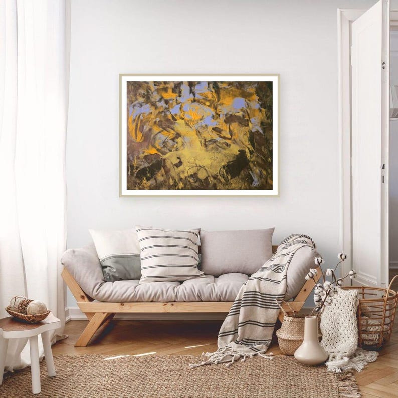 Puede incluir: Impresi&oacute;n art&iacute;stica abstracta en un marco dorado. La obra presenta una mezcla de tonos amarillos, marrones y azules. La pintura cuelga sobre un sof&aacute; de madera con cojines y una manta a rayas. Una alfombra tejida y cestas completan el interior.
