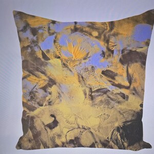 Puede incluir: Coj&iacute;n cuadrado con un dise&ntilde;o abstracto. El coj&iacute;n presenta una mezcla de colores, incluyendo amarillo, azul y marr&oacute;n, creando una apariencia texturizada y art&iacute;stica. El dise&ntilde;o se asemeja a un paisaje o una pintura de acuarela.