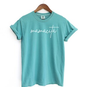 May include: A turquoise blue t-shirt with the word "mamacita" written in white cursive script.