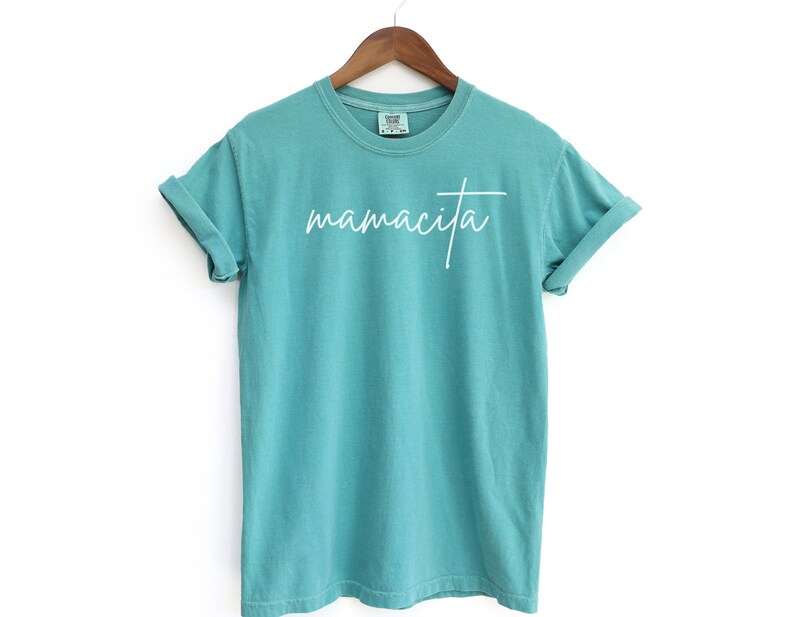 May include: A turquoise blue t-shirt with the word "mamacita" written in white cursive script.