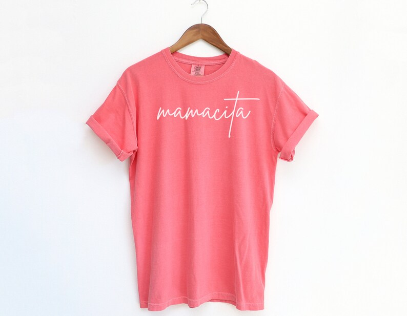 May include: A coral pink t-shirt with the word "mamacita" written in white cursive script.