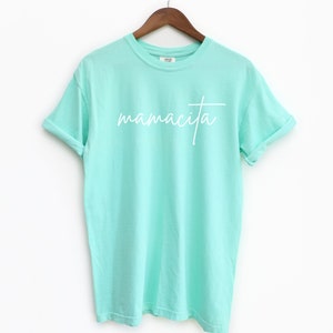 May include: A light turquoise t-shirt with the word "mamacita" written in white cursive lettering.
