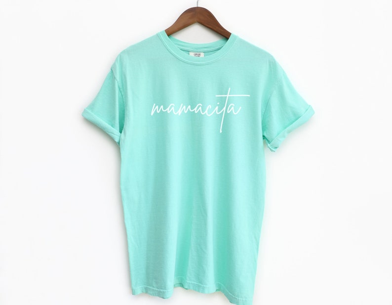 May include: A light turquoise t-shirt with the word "mamacita" written in white cursive lettering.