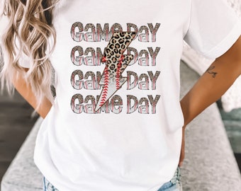 May include: White t-shirt with a graphic of a lightning bolt with a leopard print and baseball stitching. The text "Game Day" is repeated four times.
