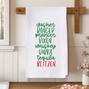 May include: White kitchen towel with green and red text that reads "dasher dancer prancer vixen whiskey vodka tequila blitzen".