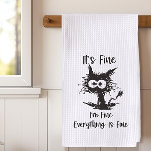 May include: White kitchen towel with a black and white illustration of a cat with the text "It's Fine I'm Fine Everything Is Fine"