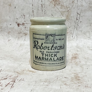 May include: An antique, off-white ceramic jar of Robertson's Thick Marmalade. The jar has a cylindrical shape with a slightly flared rim. The label features text that reads "Robertson's Old Fashioned Thick Marmalade" and mentions Paisley, Manchester, Bristol & London.