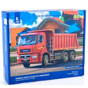 Può includere: Una scatola per un kit modello di un camion ribaltabile rosso KAMAZ-6520-21010-53. La scatola presenta un'illustrazione colorata del camion su uno sfondo di cielo blu e un edificio. Il testo sulla scatola recita "KAMAZ-6520-21010-53 SAMOSVAL" e "KAMAZ-6520-21010-53 TIPPER".